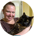 A woman gently cradles a cat in her arms, smiling warmly at the camera